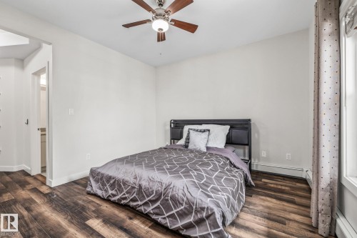 This room features rich wood-look flooring, a ceiling fan with integrated lighting, and a window with curtains - 212 10611 117 Street, Edmonton, AB - Indoor Photo Showing Bedroom