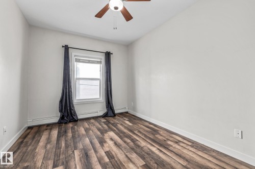 Room featuring wood-look flooring, a window with dark curtains, and a ceiling fan with integrated lighting - 212 10611 117 Street, Edmonton, AB - Indoor Photo Showing Other Room