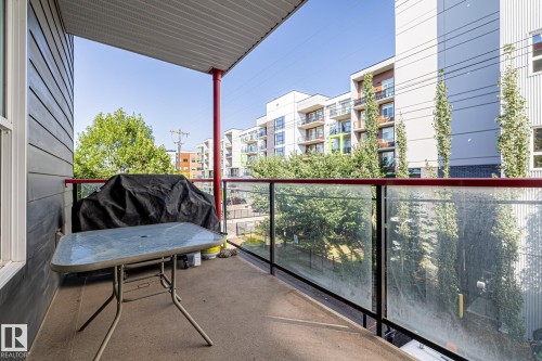 The property features a balcony with a concrete floor and a glass railing, offering views of the surrounding buildings and trees - 212 10611 117 Street, Edmonton, AB - Outdoor With Balcony With Exterior