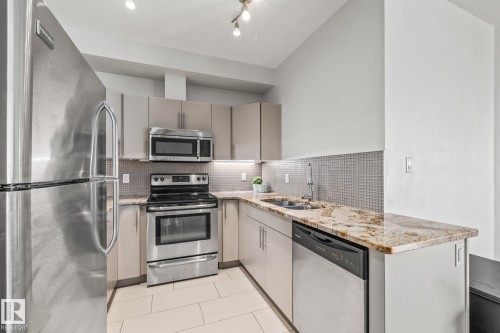The kitchen features stainless steel appliances, granite countertops, and a tile backsplash - 212 10611 117 Street, Edmonton, AB - Indoor Photo Showing Kitchen With Double Sink With Upgraded Kitchen