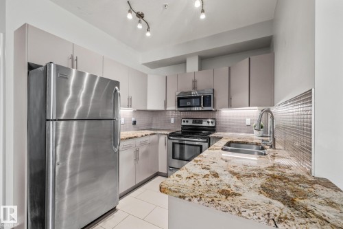 The kitchen features stainless steel appliances, granite countertops, and light-colored cabinetry - 212 10611 117 Street, Edmonton, AB - Indoor Photo Showing Kitchen With Double Sink With Upgraded Kitchen