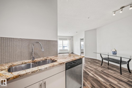 The kitchen features a double stainless steel sink with a high arc faucet, granite countertops, and a mosaic tile backsplash - 212 10611 117 Street, Edmonton, AB - Indoor Photo Showing Kitchen With Double Sink