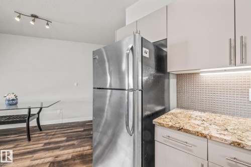 The kitchen features a stainless steel refrigerator, light-colored cabinetry, and a granite countertop - 212 10611 117 Street, Edmonton, AB - Indoor Photo Showing Kitchen