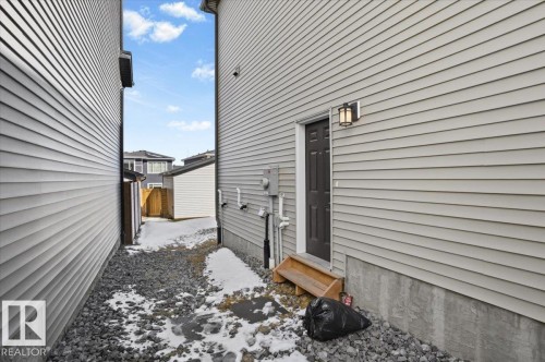 The property features light-colored horizontal siding, a dark entry door with a wooden step, and an exterior light fixture - 204 Charlesworth Drive, Edmonton, AB - Outdoor With Exterior