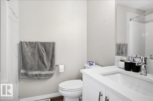 The bathroom features a modern vanity with a white countertop and an integrated sink, a toilet, and a shower area with white marble-patterned wall tiles - 204 Charlesworth Drive, Edmonton, AB - Indoor Photo Showing Bathroom
