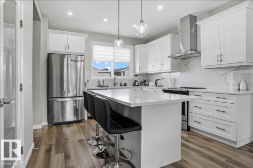 The kitchen features white cabinetry, stainless steel appliances, and a central island with bar seating - 204 Charlesworth Drive, Edmonton, AB - Indoor Photo Showing Kitchen With Upgraded Kitchen