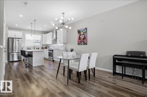 This open-concept area features hardwood flooring, a modern white kitchen with stainless steel appliances, and a dining space illuminated by a contemporary chandelier - 204 Charlesworth Drive, Edmonton, AB - Indoor