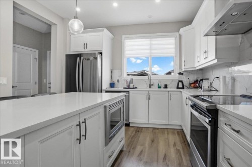 The kitchen features white cabinetry, stainless steel appliances, a center island with an integrated microwave, and light-colored countertops - 204 Charlesworth Drive, Edmonton, AB - Indoor Photo Showing Kitchen With Stainless Steel Kitchen With Upgraded Kitchen