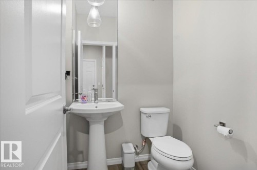 This powder room features a white pedestal sink with a mirror and a white toilet - 204 Charlesworth Drive, Edmonton, AB - Indoor Photo Showing Bathroom