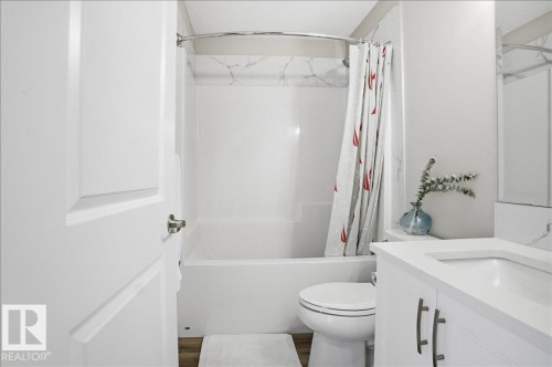 This bathroom features a white bathtub with a shower, a toilet, and a vanity with a sink and white countertop - 204 Charlesworth Drive, Edmonton, AB - Indoor Photo Showing Bathroom