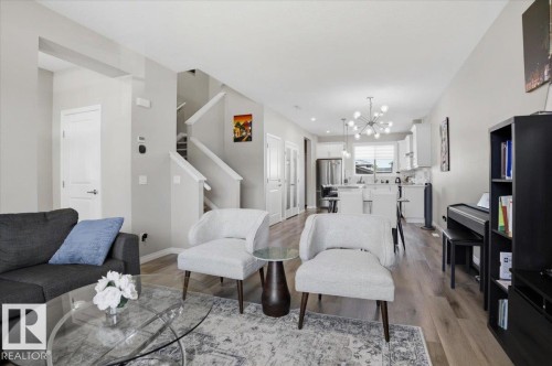 The living area features light-toned walls, hardwood style flooring, and a view into the kitchen with white cabinetry and stainless steel appliances - 204 Charlesworth Drive, Edmonton, AB - Indoor Photo Showing Living Room