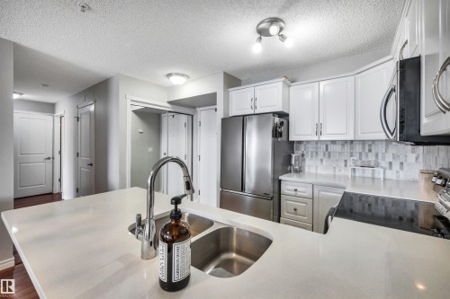 The kitchen features white cabinetry, stainless steel appliances, a tile backsplash, and a double basin sink set into a light-colored countertop - 319 17404 64 Avenue, Edmonton, AB - Indoor Photo Showing Kitchen With Double Sink