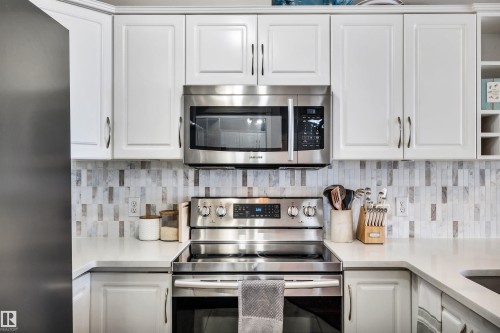 The kitchen features white cabinetry, a tiled backsplash, and stainless steel appliances, including a microwave and range - 319 17404 64 Avenue, Edmonton, AB - Indoor Photo Showing Kitchen