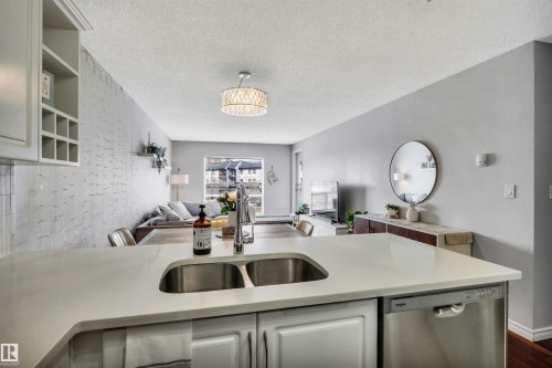 The kitchen features a double stainless steel sink and a stainless steel dishwasher, integrated into a light-toned countertop - 319 17404 64 Avenue, Edmonton, AB - Indoor Photo Showing Kitchen With Double Sink
