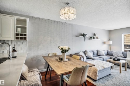 Open concept living area featuring hardwood flooring, a dining table with seating, a spacious sectional sofa, and a modern chandelier - 319 17404 64 Avenue, Edmonton, AB - Indoor