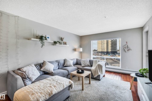 Living area featuring light-colored walls, wood flooring, and a large window with blinds providing natural light - 319 17404 64 Avenue, Edmonton, AB - Indoor Photo Showing Living Room