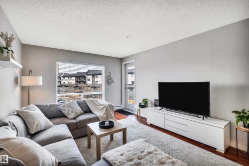 Spacious living area featuring hardwood floors, a large window with blinds, and a door providing exterior access - 319 17404 64 Avenue, Edmonton, AB - Indoor Photo Showing Living Room