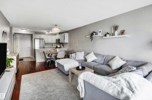 The property features an open-concept living area with dark hardwood flooring, a modern kitchen with white cabinetry and stainless steel appliances, and a dedicated dining space - 319 17404 64 Avenue, Edmonton, AB - Indoor Photo Showing Living Room