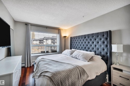 This room features hardwood flooring, a window with horizontal blinds and curtains, and a textured ceiling - 319 17404 64 Avenue, Edmonton, AB - Indoor Photo Showing Bedroom