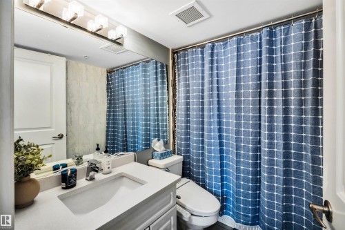 Bathroom featuring a white vanity with an integrated sink, a large mirror, and overhead lighting - 319 17404 64 Avenue, Edmonton, AB - Indoor Photo Showing Bathroom
