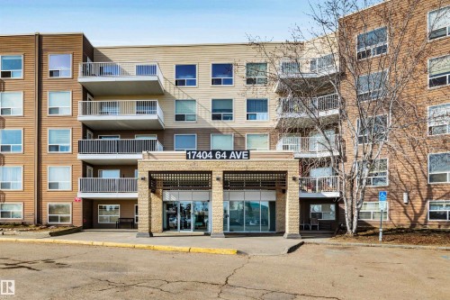 The property features a multi-story building with a prominent main entrance, balconies with railings, and a mix of tan and brown exterior siding - 319 17404 64 Avenue, Edmonton, AB - Outdoor With Balcony With Facade