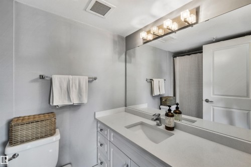 The bathroom features a vanity with a white countertop and an integrated sink, illuminated by a light fixture with six clear glass shades - 319 17404 64 Avenue, Edmonton, AB - Indoor Photo Showing Bathroom