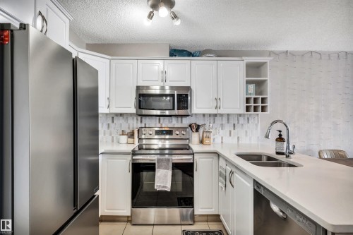 Kitchen featuring white cabinetry, stainless steel appliances, a double basin sink, and a tiled backsplash - 319 17404 64 Avenue, Edmonton, AB - Indoor Photo Showing Kitchen With Double Sink With Upgraded Kitchen