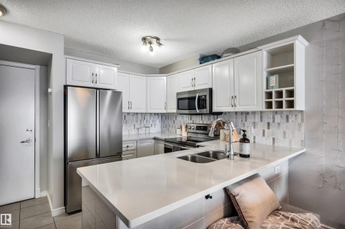 The kitchen features white cabinetry, stainless steel appliances, and a light-colored countertop - 319 17404 64 Avenue, Edmonton, AB - Indoor Photo Showing Kitchen With Double Sink With Upgraded Kitchen