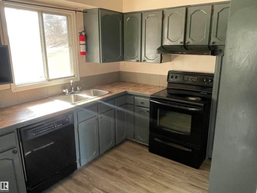 The kitchen features dark cabinetry, a double basin sink, a black dishwasher, and a black electric range with an overhead exhaust fan - 12335 132 Avenue, Edmonton, AB - Indoor Photo Showing Kitchen With Double Sink