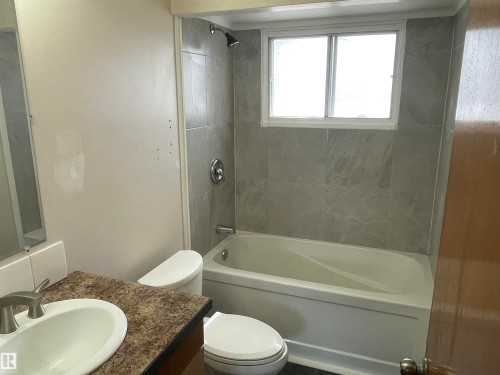 The bathroom features a tiled shower and bath with a window, a toilet, and a vanity with a sink - 12335 132 Avenue, Edmonton, AB - Indoor Photo Showing Bathroom