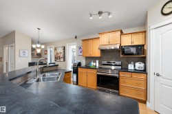 The kitchen features light wood cabinetry, stainless steel appliances, and dark countertops - 