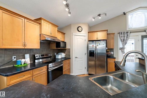 The kitchen features ample cabinetry, dark countertops, a stainless steel refrigerator, and a double basin sink with a high arc faucet - 16748 118 Street, Edmonton, AB - Indoor Photo Showing Kitchen With Double Sink