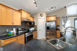 The kitchen features ample cabinetry, dark countertops, a stainless steel refrigerator, and a double basin sink with a high arc faucet - 