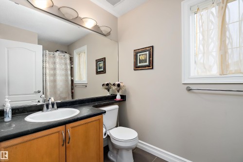 Bathroom featuring a vanity with a light wood cabinet and dark countertop, an oval sink, a toilet, and a window providing natural light - 16748 118 Street, Edmonton, AB - Indoor Photo Showing Bathroom