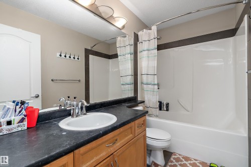 The bathroom features a light brown vanity with a black countertop, a white oval sink with a chrome faucet, and a large mirror - 16748 118 Street, Edmonton, AB - Indoor Photo Showing Bathroom