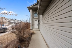 The property features a concrete walkway leading to the front entrance, which includes a white door with a window and an overhead light fixture - 