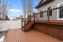 Outdoor deck space featuring wooden decking, a staircase with dark wood railings and balusters, and a white fence - 