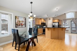 This open-concept living space features light-toned hardwood flooring, a kitchen island with a dark countertop, and warm wood cabinetry - 