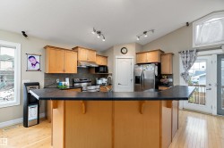 Kitchen featuring a breakfast bar with a dark countertop, light wood cabinetry, stainless steel appliances, and hardwood flooring - 