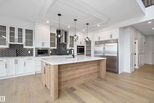 The kitchen features light wood flooring, white cabinetry, a dark herringbone tile backsplash, and a light wood kitchen island with a white countertop - 34 Cannes Cove, St. Albert, AB - Indoor Photo Showing Kitchen With Upgraded Kitchen
