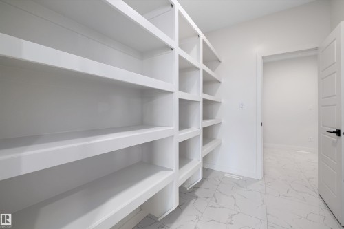 This space features extensive built-in shelving, white walls, and a white tile floor with grey veining - 34 Cannes Cove, St. Albert, AB - Indoor With Storage