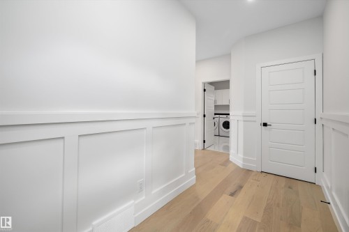 Hallway featuring light-toned flooring, white paneling, and a modern white door with a black handle - 34 Cannes Cove, St. Albert, AB - Indoor Photo Showing Other Room