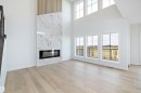 The living area features a modern linear fireplace with a marble-style surround, light wood flooring, and tall windows providing ample natural light - 34 Cannes Cove, St. Albert, AB  - Indoor Photo Showing Living Room With Fireplace 