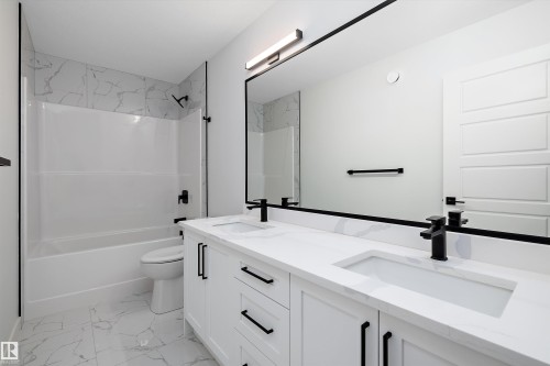 The bathroom features a double vanity with white cabinetry and black hardware, a black-framed mirror, and a white bathtub with a tile surround - 34 Cannes Cove, St. Albert, AB - Indoor Photo Showing Bathroom