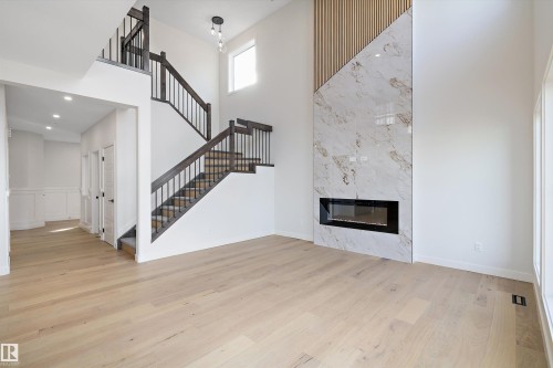 The property features light wood flooring, a fireplace with a light marble surround, and a staircase with dark wood handrails and black balusters - 34 Cannes Cove, St. Albert, AB - Indoor With Fireplace