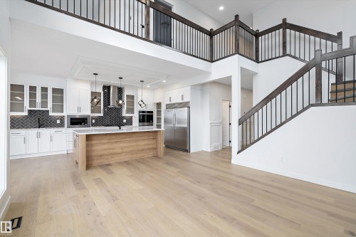 Open concept interior featuring hardwood floors, a kitchen with white cabinetry and a light wood island, and a staircase with dark wood railings - 34 Cannes Cove, St. Albert, AB - Indoor Photo Showing Other Room