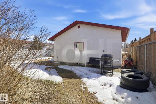 The property features a stucco exterior with a red trim roof, a backyard area with patches of grass and snow, and a chain link fence - 4129 134A Avenue Nw, Edmonton, AB - Outdoor With Exterior