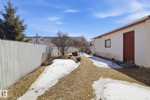 The property features an exterior building with a red door and a small window, set within a yard that includes a pathway, patches of grass, and areas of snow - 4129 134A Avenue Nw, Edmonton, AB - Outdoor