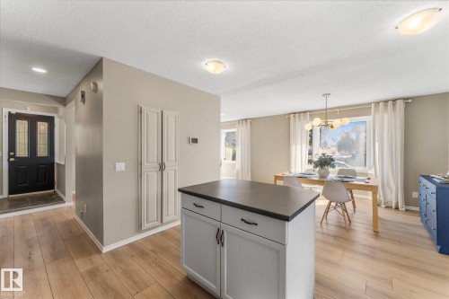The property features wood flooring, a central island with storage, and a dining area with a modern chandelier and large windows - 2626 49 Street, Edmonton, AB - Indoor