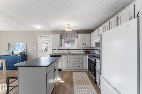 The kitchen features light-toned cabinetry with dark hardware, a center island with a dark countertop, and light wood flooring - 2626 49 Street, Edmonton, AB - Indoor Photo Showing Kitchen